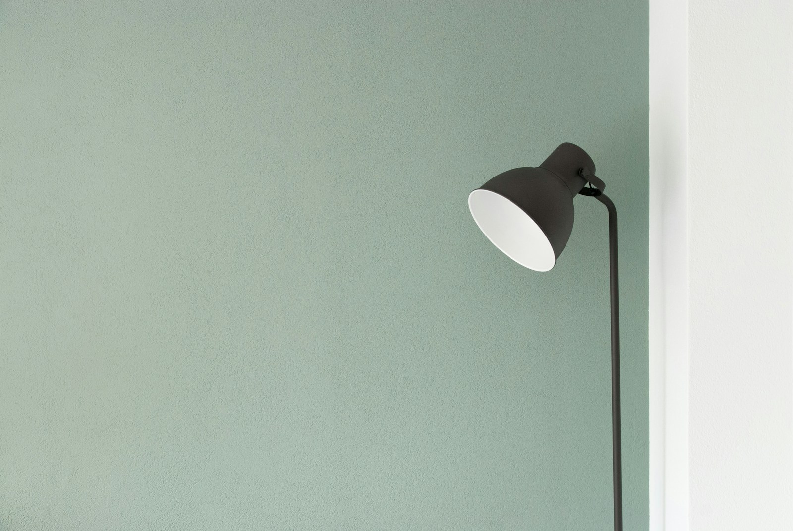 Simple metal reading lamp against a muted green wall